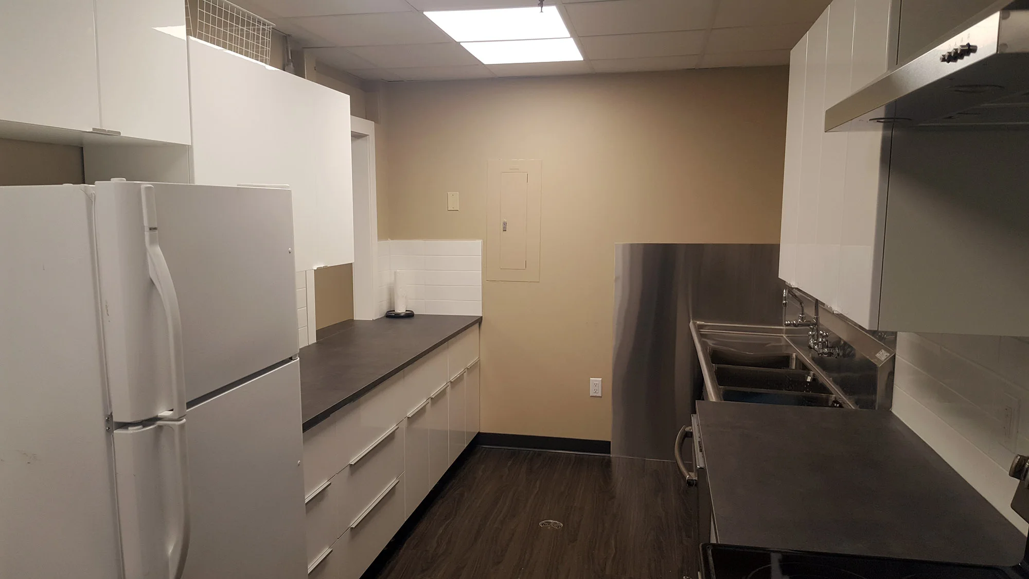 Finished community kitchen renovation in Calgary — the commercial-grade three-bowl stainless sink and stainless backsplash, August 2017