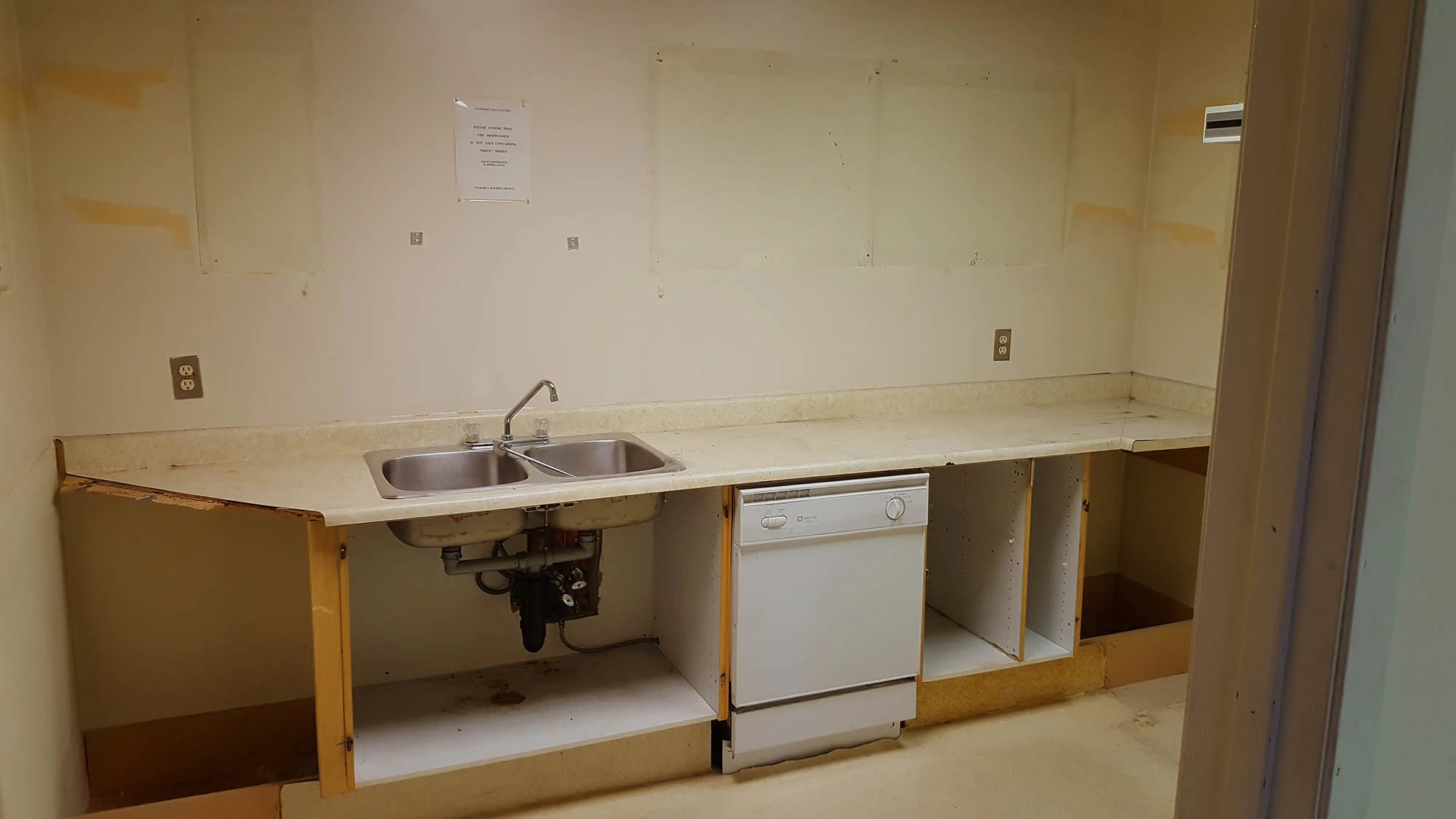 Community kitchen renovation in Calgary, before — the original galley kitchen with a double sink and stripped cabinets, July 2017