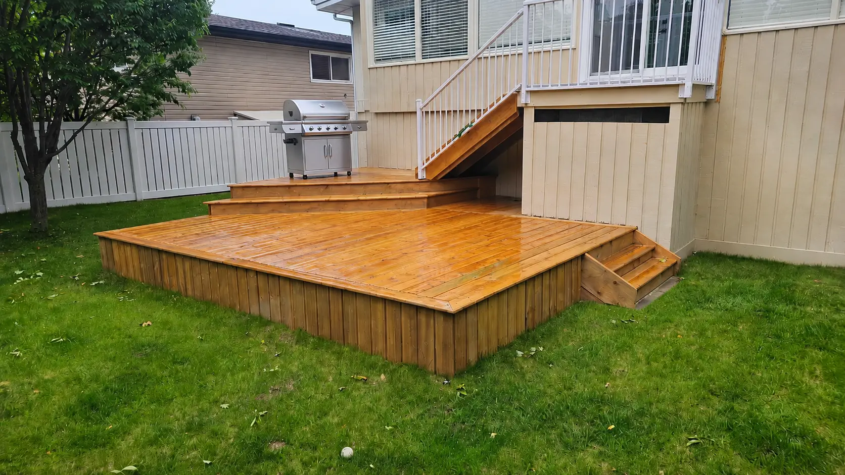 A two-tier wood deck with skirting and wide steps to the lawn, built in University Heights, Calgary