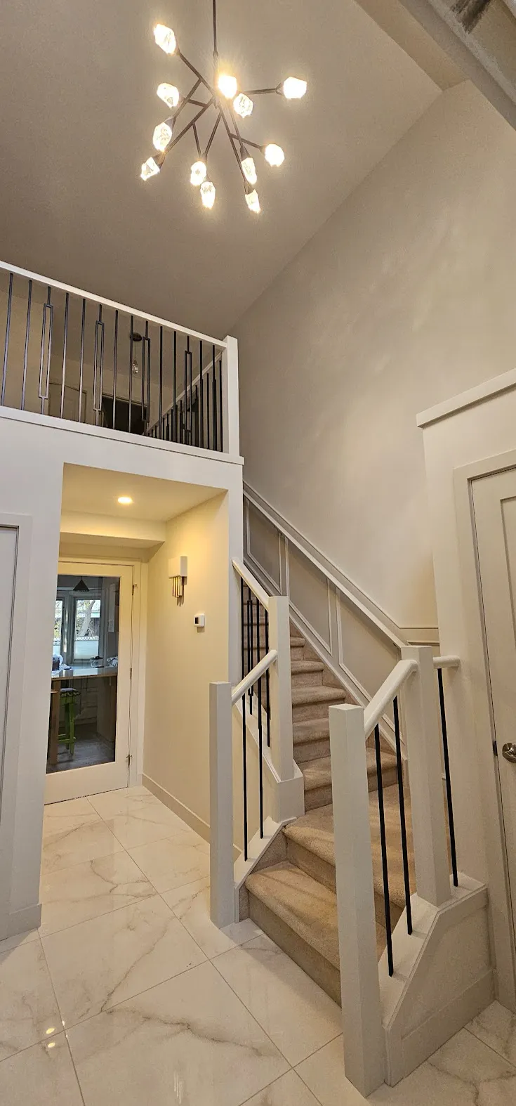 Lake Bonavista home entry after renovation — marble-look tile, a carpeted staircase with black iron spindles and a modern chandelier, Calgary