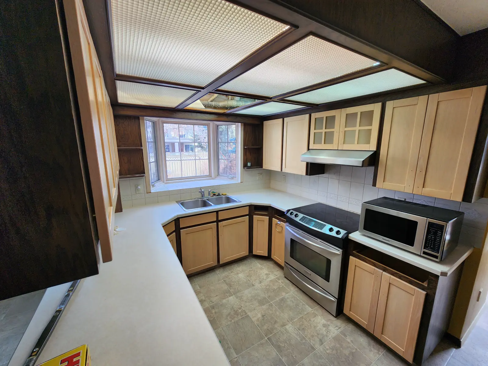 Lake Bonavista kitchen before renovation — a dark-wood ceiling light box, pale maple cabinets and tile floor, Calgary