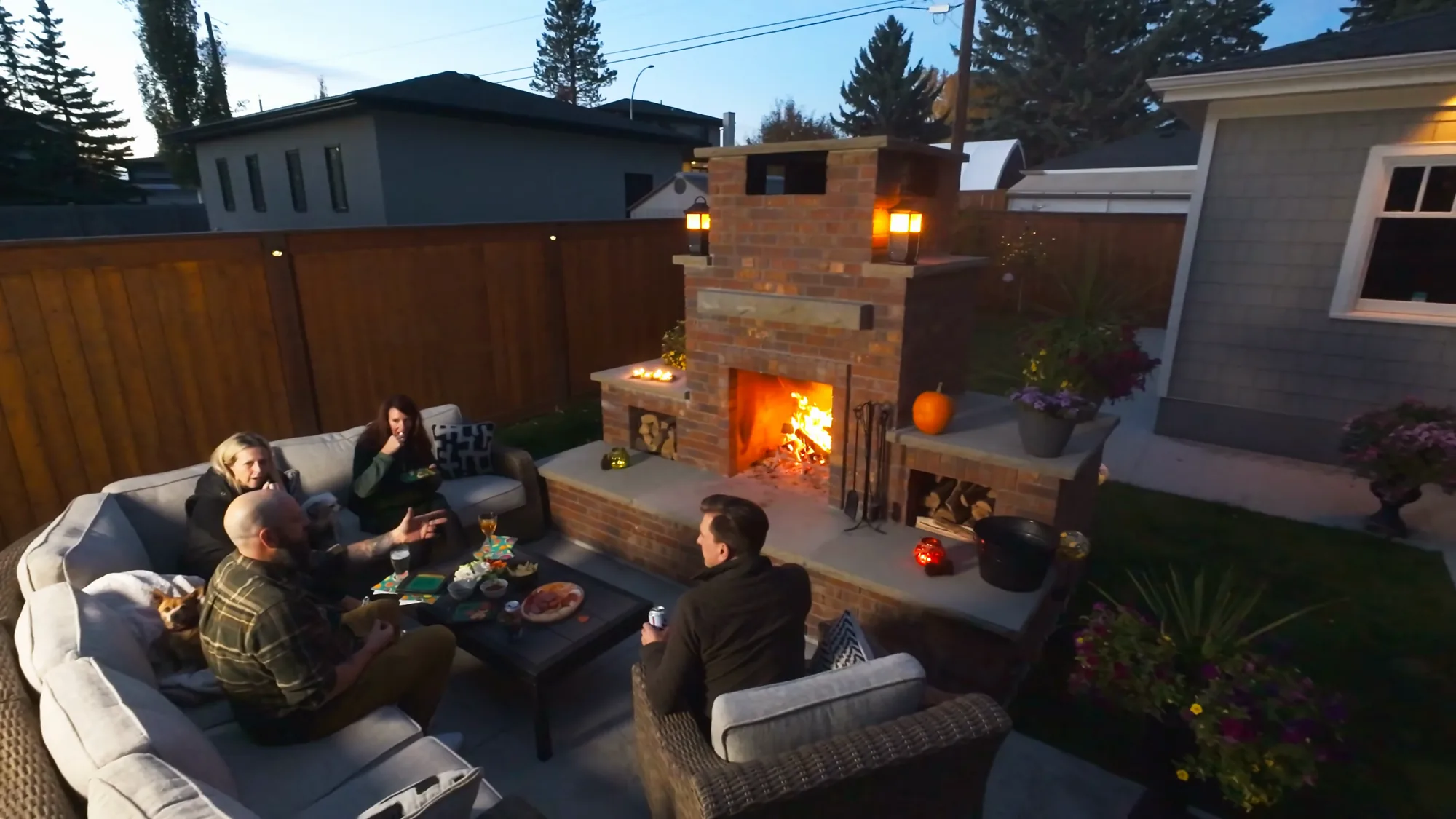 Overhead evening view of four people seated around a burning backyard hearth on a concrete patio, Calgary