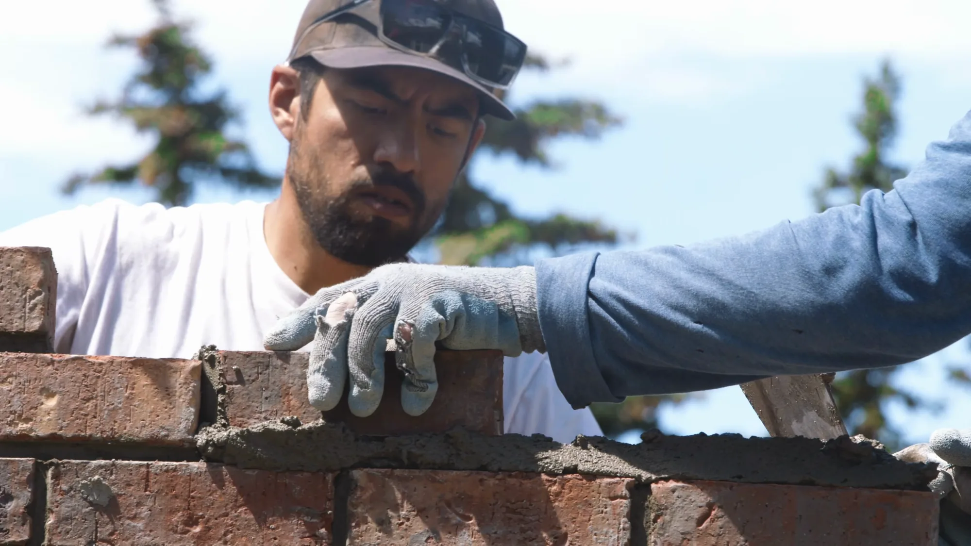 Bricklayer pressing a clay brick into a fresh bed under a summer sky, northwest Calgary