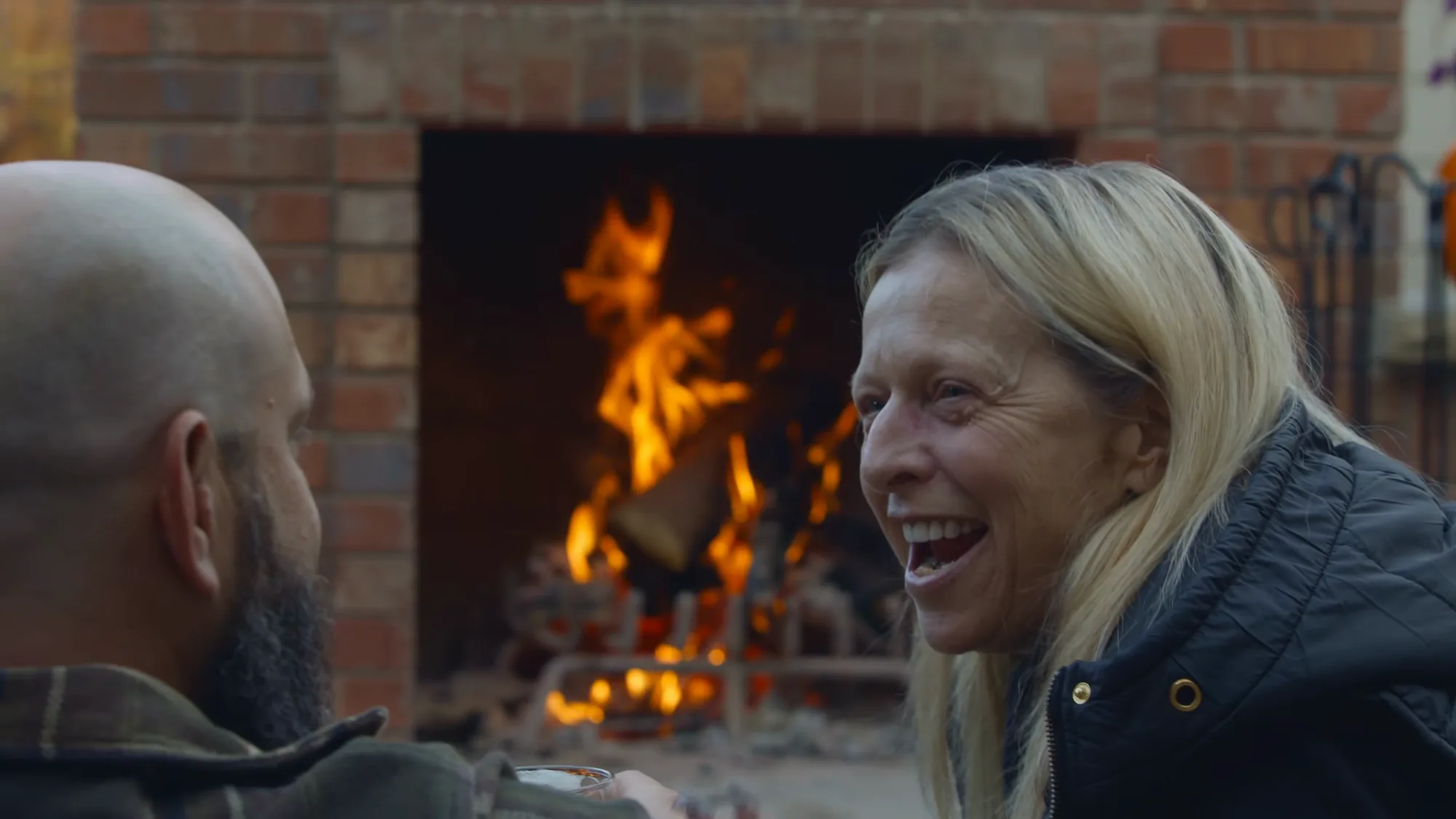 Two guests laughing beside the open firebox and iron grate as the fire burns, Montgomery