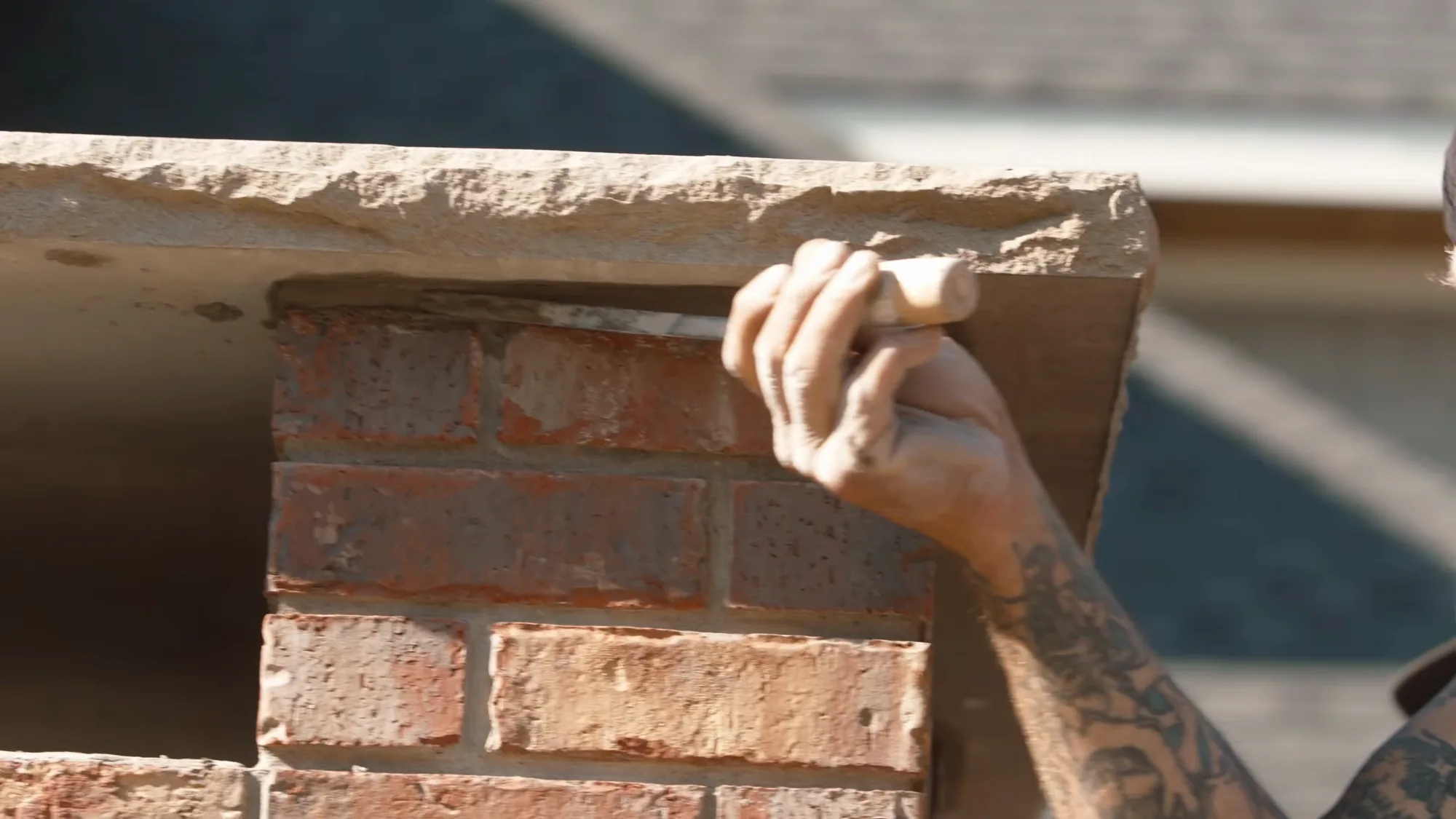 Bare hand guiding a chiselled cast concrete ledge down onto the brick coursing, Calgary