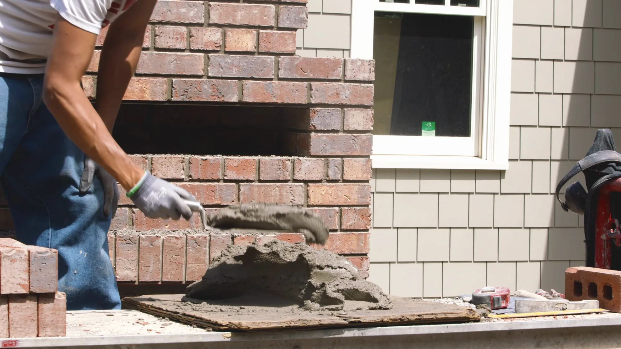 Mason turning mortar with a trowel on a board beside the part built firebox and chimney, Calgary