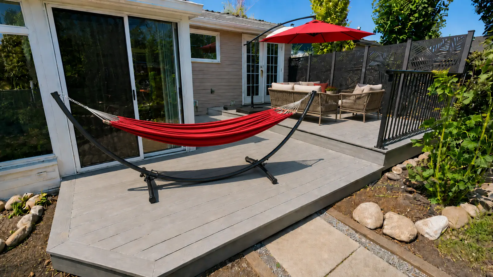 Okotoks back deck after renovation — grey composite decking with a hammock, an outdoor lounge under a red umbrella and laser-cut privacy screens, Calgary