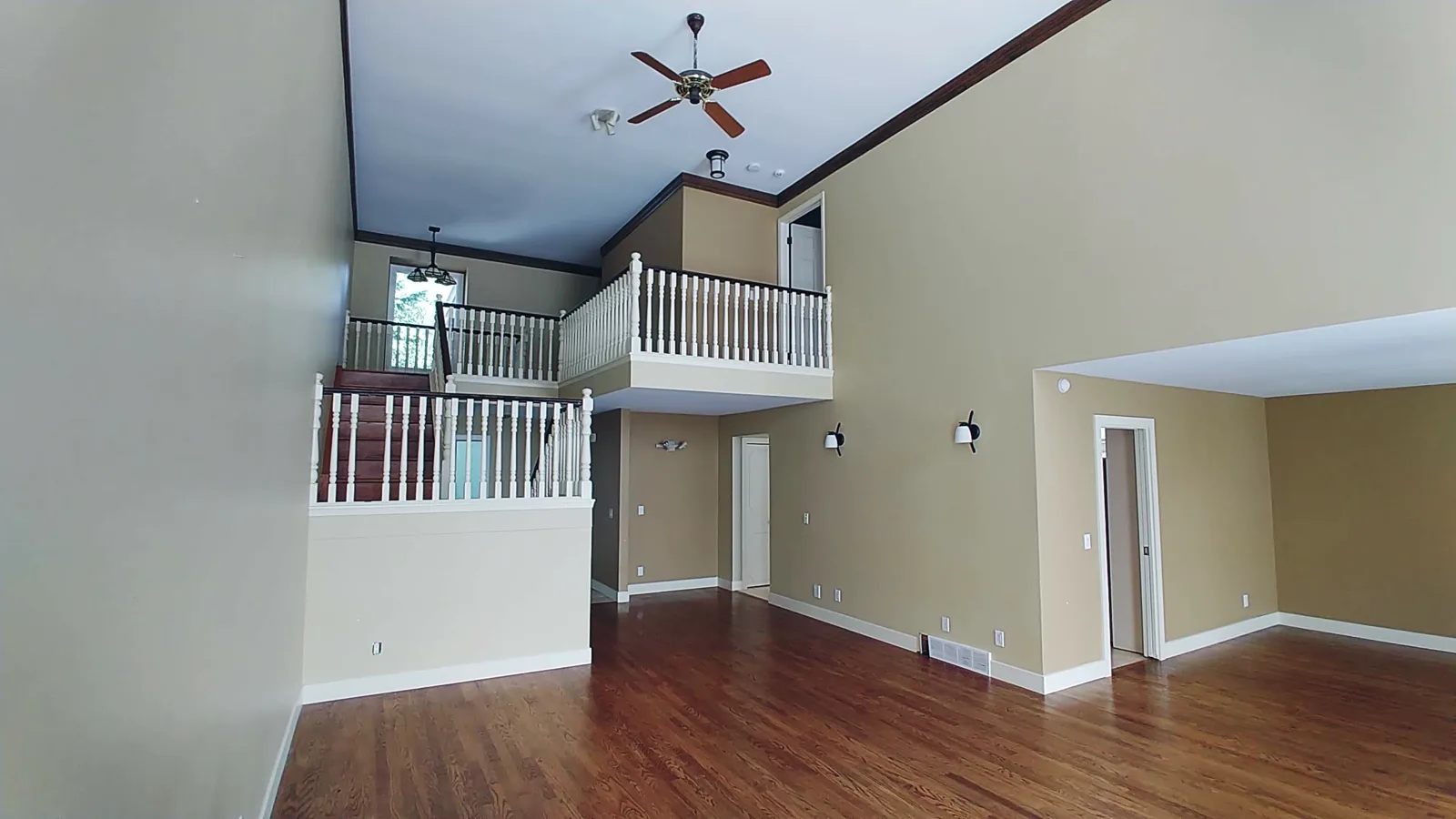 Rideau great room before renovation — a dark cherry staircase with white colonial spindles and a wood ceiling fan under a vaulted ceiling, Calgary