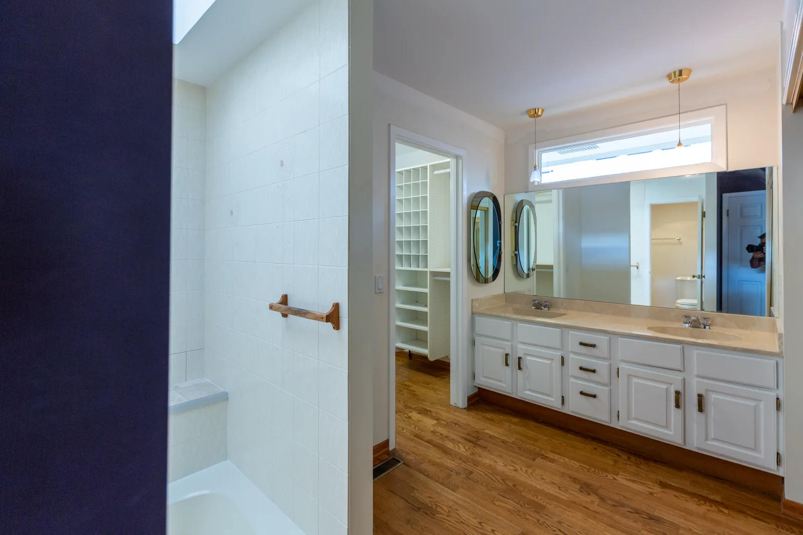 Rideau primary ensuite before renovation — a navy accent wall, white raised-panel double vanity and two oval tilting mirrors, Calgary