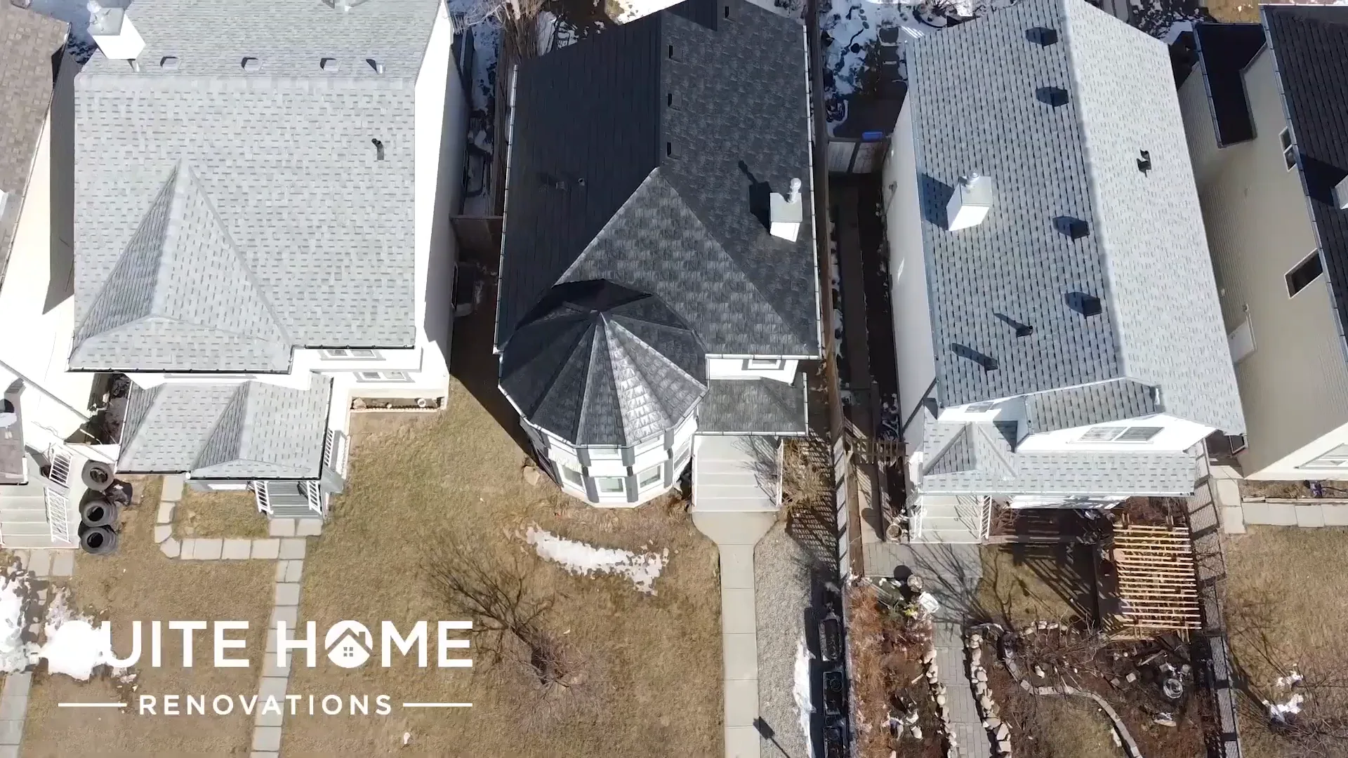 Overhead aerial of the completed dark rubber slate roof and octagonal turret among pale grey asphalt neighbouring roofs in northeast Calgary