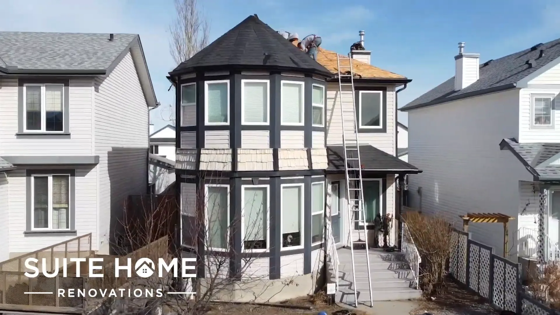 Two storey Calgary home with an octagonal bay tower, original asphalt shingle roof and a ladder up to the roofline at the start of the tear-off