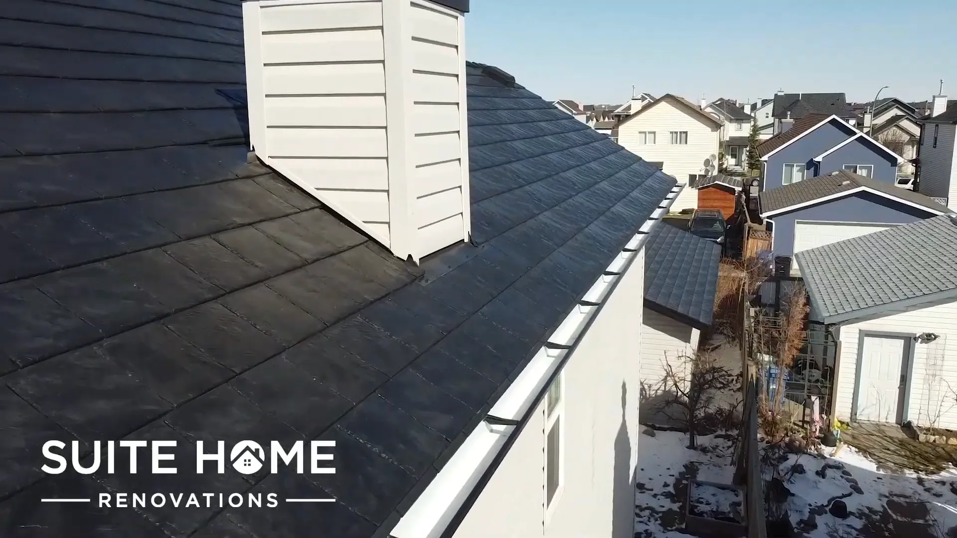 Finished dark rubber slate roof running to the ridge beside a cream sided chimney chase on a Calgary home