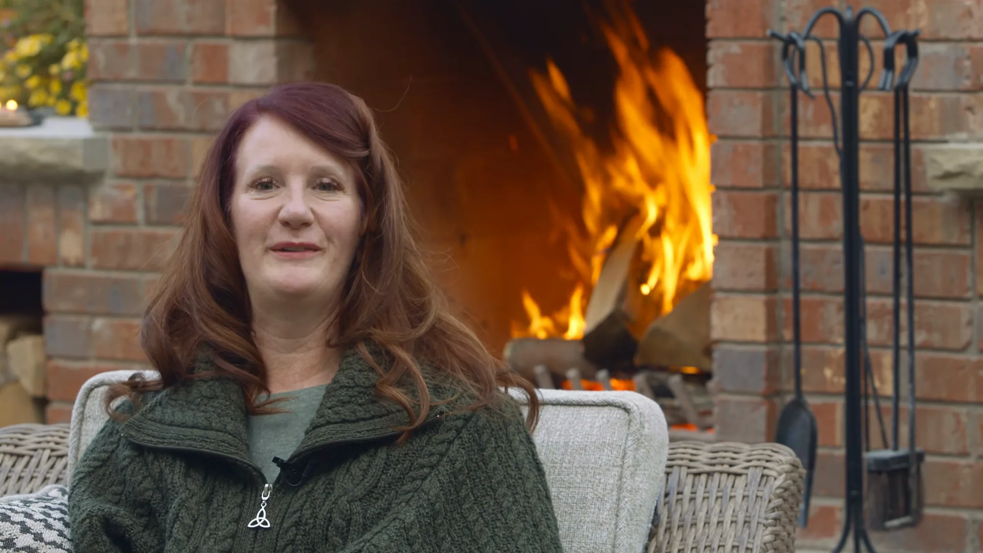 Calgary homeowner sitting beside her finished backyard fireplace, talking to camera as the fire burns